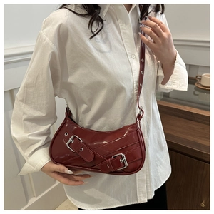 Close-up of wine red crescent shoulder bag featuring double belt buckles and silver hardware