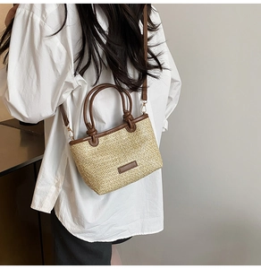Detail of woven straw bucket bag showing leather handles and adjustable shoulder strap