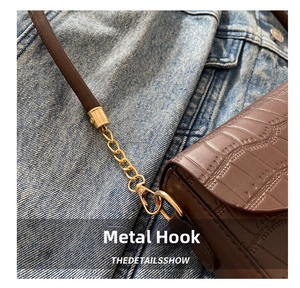 Detail von Goldmetallhaken und Kette an brauner Lederhandtasche mit Krokostruktur