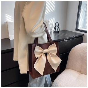 Detail view of large brown tote bag with cream bow accent worn on model shoulder