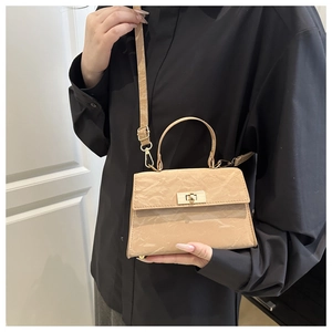 Close-up of beige textured crossbody bag with gold twist lock and fine stitching