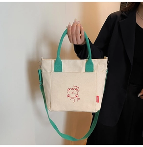 Detail of beige canvas tote with green handles, bear print, and metal shoulder strap clip