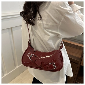 Detail of dark red crescent shoulder bag featuring crisscross straps and metal buckles