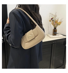 Chic beige half-moon shoulder bag featuring a stylish golden bow clasp detail