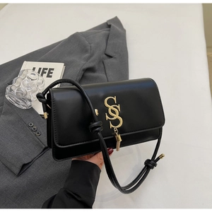 Close-up of black leather crossbody bag with gold metal logo and knotted strap detail