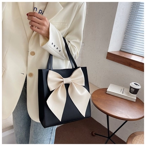 Detail of a black leather tote bag featuring a large cream bow in a cozy indoor setting