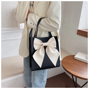 Detail of a large black tote bag featuring a prominent cream bow on a smooth leather surface