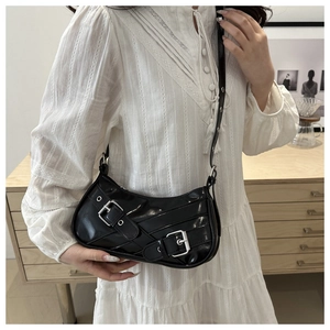 Detail of black glossy crescent bag with silver buckles worn over a white dress