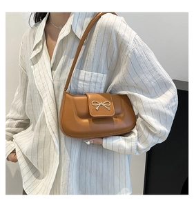 Close-up of caramel brown shoulder bag featuring a metallic gold bow buckle and leather texture
