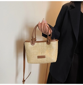 Detail of woven straw bucket bag featuring a brown leather knot handle and shoulder strap
