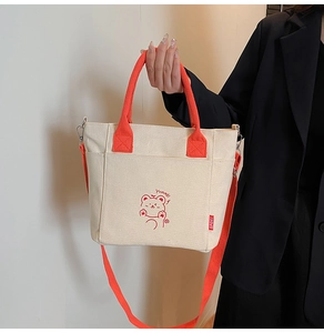 Detail of cream canvas bag featuring orange handles and cute cartoon bear print