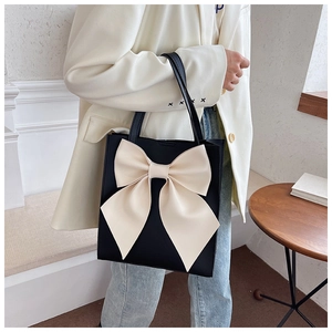 Detail view of large black tote bag with oversized white bow and long shoulder straps