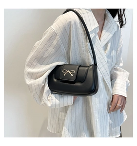 Detail of minimalist black leather underarm bag with gold bow clasp and shoulder strap