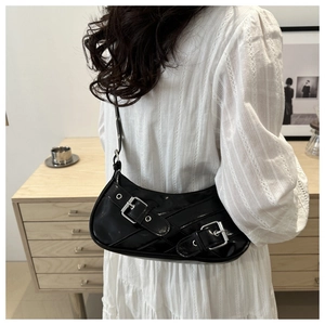 Detail of black patent leather crescent bag with silver buckles and studs on model