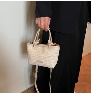 Dettaglio borsa a secchiello in paglia intrecciata con manico in pelle color crema
