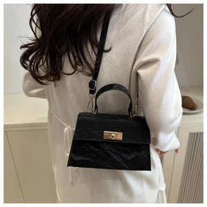 Detail of a black textured leather crossbody bag with a gold clasp on a model