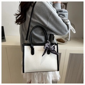 Detailed view of white snakeskin texture tote with fashion text and checkered scarf bow