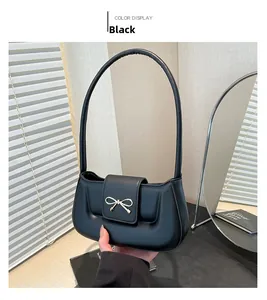 Detail of a black PU leather handbag with a golden bow-shaped metal clasp and shoulder strap