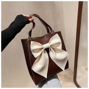 Detail of a brown leather tote bag featuring a large three-dimensional cream bow decoration