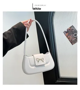 Detail of white PU leather shoulder bag featuring a gold metal bow buckle and flap closure