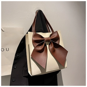 Detailed view of the large brown decorative bow on a cream-colored tote handbag