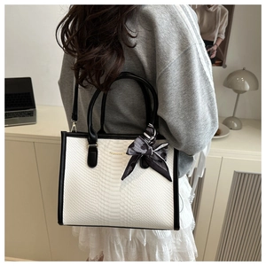 Detail of white crocodile pattern tote bag with floral ribbon and metal hardware on handle