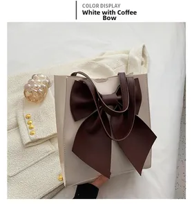 Detail of off-white tote bag featuring a large dark brown bow and leather texture