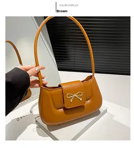 Detail of caramel brown underarm bag with signature golden metal bow on white stand