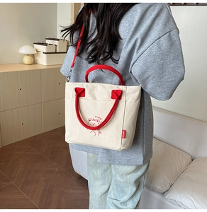 Model wearing a cream canvas bucket bag with red straps and cute bear illustration