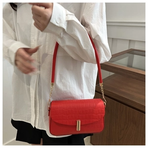 Detail of red croc-embossed shoulder bag with gold clasp and chain strap on model