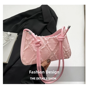 Detail of pink denim underarm bag featuring fringe edges and woven knot shoulder strap