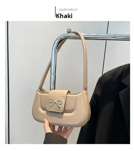 Detail of khaki shoulder bag featuring a decorative metal bow clasp and sleek leather finish