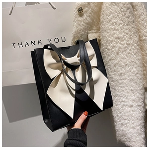 Detail of a large black tote bag with white bow and textured leather for women
