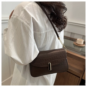 Detail of a brown crocodile pattern shoulder bag with a gold metal lock and leather strap