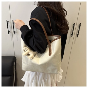 Détail d'un sac cabas patchwork blanc crème avec des sangles brunes et un petit charme