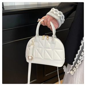 Detail of white shell handbag featuring quilted patterns and gold metal zippers