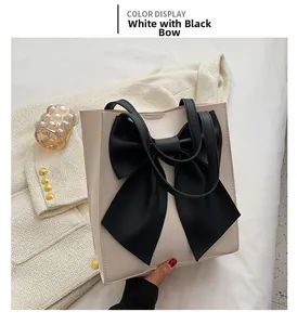 Detail of large beige tote bag featuring a prominent black bow and slender handle straps