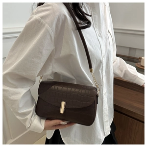 Detail einer dunkelbraunen Handtasche mit Krokodilmuster, Goldverschluss und Kette