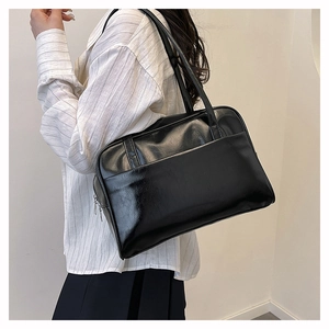 Close-up of a black glossy leather shoulder bag featuring a wide pocket and metal zipper
