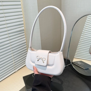 Minimalist white shoulder bag with silver bow accent and slim strap on a decorative desk