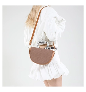 Détail du sac selle avec bordure en cuir marron, texture tissée et poignée en métal argenté