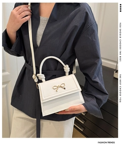 Detail of white mini bag with golden bow lock and twisted handle on blue shirt