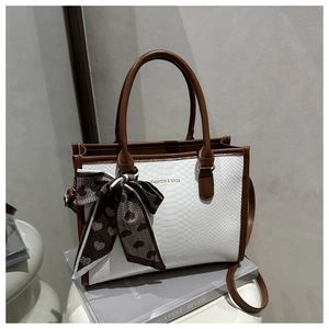 Detail of white snakeskin tote bag with brown handles and heart print silk scarf ribbon