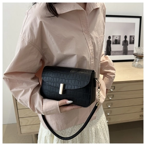 Detail of a black faux-leather shoulder bag with crocodile texture and gold metal buckle
