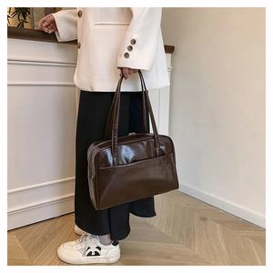 Detailed view of large dark brown patent leather tote bag carried on woman's shoulder