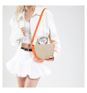 Détail d'un sac selle orange vif avec rabat tissé beige et une poignée ronde en métal argenté