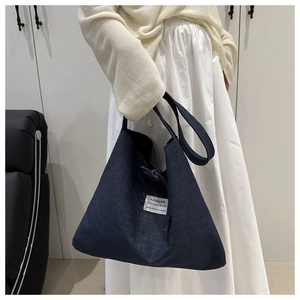 Detail of blue denim patchwork tote bag with fashion label held by model in knitwear