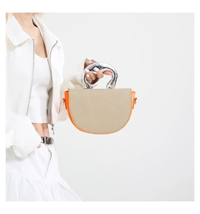 Détail du sac selle en cuir orange avec texture tissée beige et poignée en métal argenté