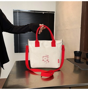 Detail of red handles and adjustable strap on a canvas bucket tote bag with bear design