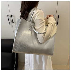 Détail d'un sac cabas argenté avec motif crocodile et poignées rondes en métal